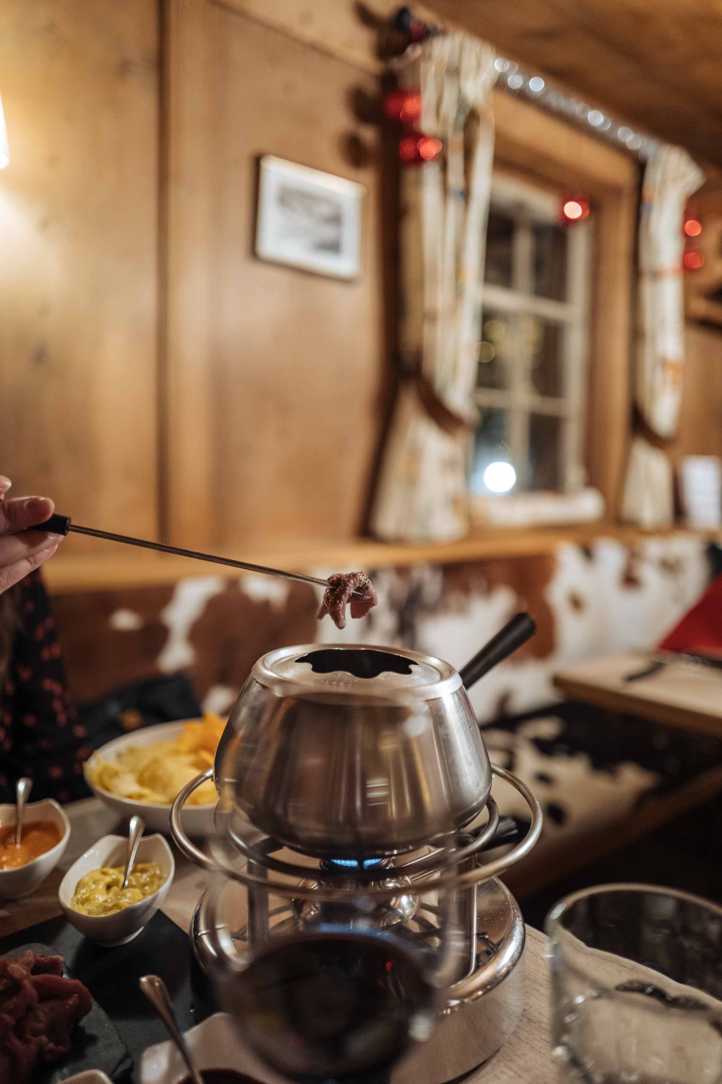 Dip meat into a bubbling pot of broth with this Chinoise fondue dinner, similar to a hot pot. Here’s where to go for the best fondue or raclette dinner in Klosters. Use our guide to know where to go and the best restaurants to find that and fondue with our guide to Klosters. | thetasteedit.com #travel #switzerland #winter #food #fondue