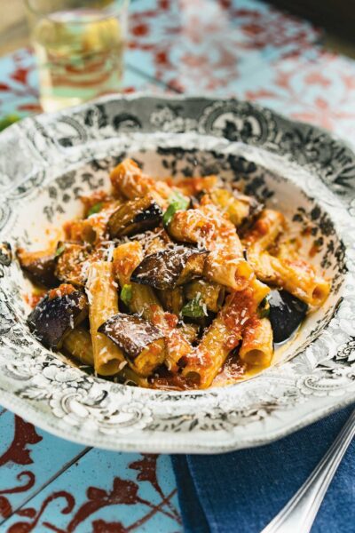 Delicious Sicilian Pasta alla Norma with fried eggplant and grated cheese on an ornate plate, ready to be served.