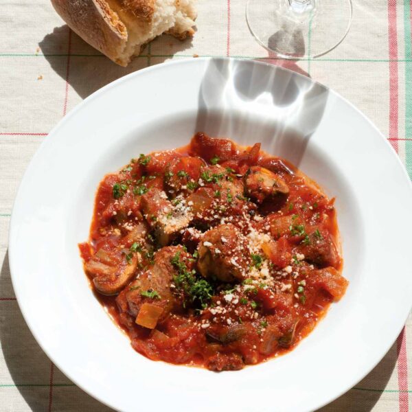 Mouthwatering plate of Carmine's mushroom and sausage stew, garnished with parsley and parmesan, paired with crusty bread and a glass of red wine, from WM Brown's 'A Man and His Kitchen' cookbook' by Matt Hranek