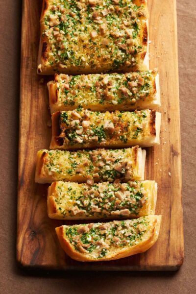 Savory City Island's clam garlic bread slices, topped with fresh herbs and diced clams, presented on a rustic wooden board, from WM Brown's 'A Man and His Kitchen' book.