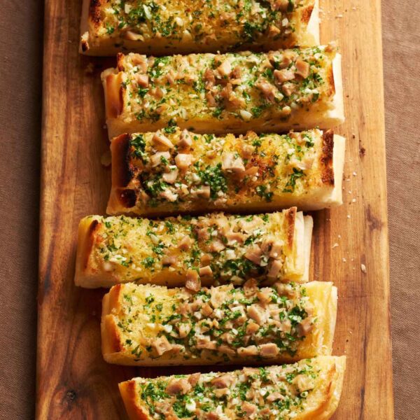 Savory City Island's clam garlic bread slices, topped with fresh herbs and diced clams, presented on a rustic wooden board, from WM Brown's 'A Man and His Kitchen' book.