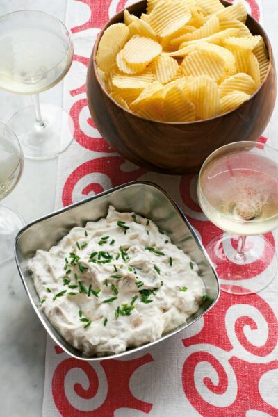 Delicious bowl of Edward's Christmas family clam dip, topped with fresh chives, served alongside golden potato chips and glasses of white wine, from WM Brown's 'A Man and His Kitchen' cookbook.
