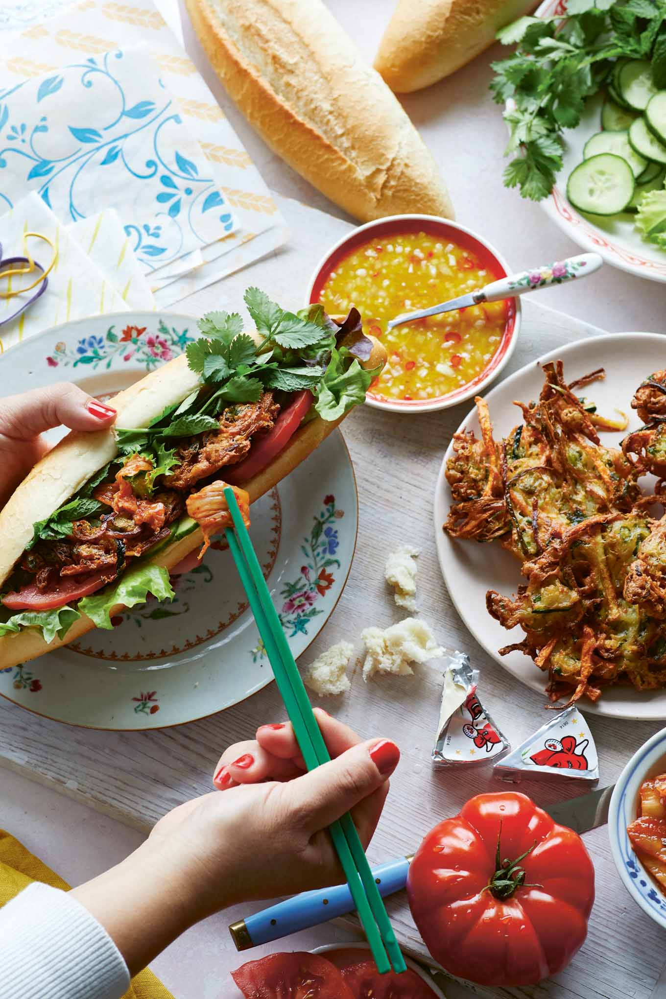 Crispy lemongrass and vegetable fritter sandwich with fresh herbs, kimchi, and crusty baguette, served alongside dipping sauce.