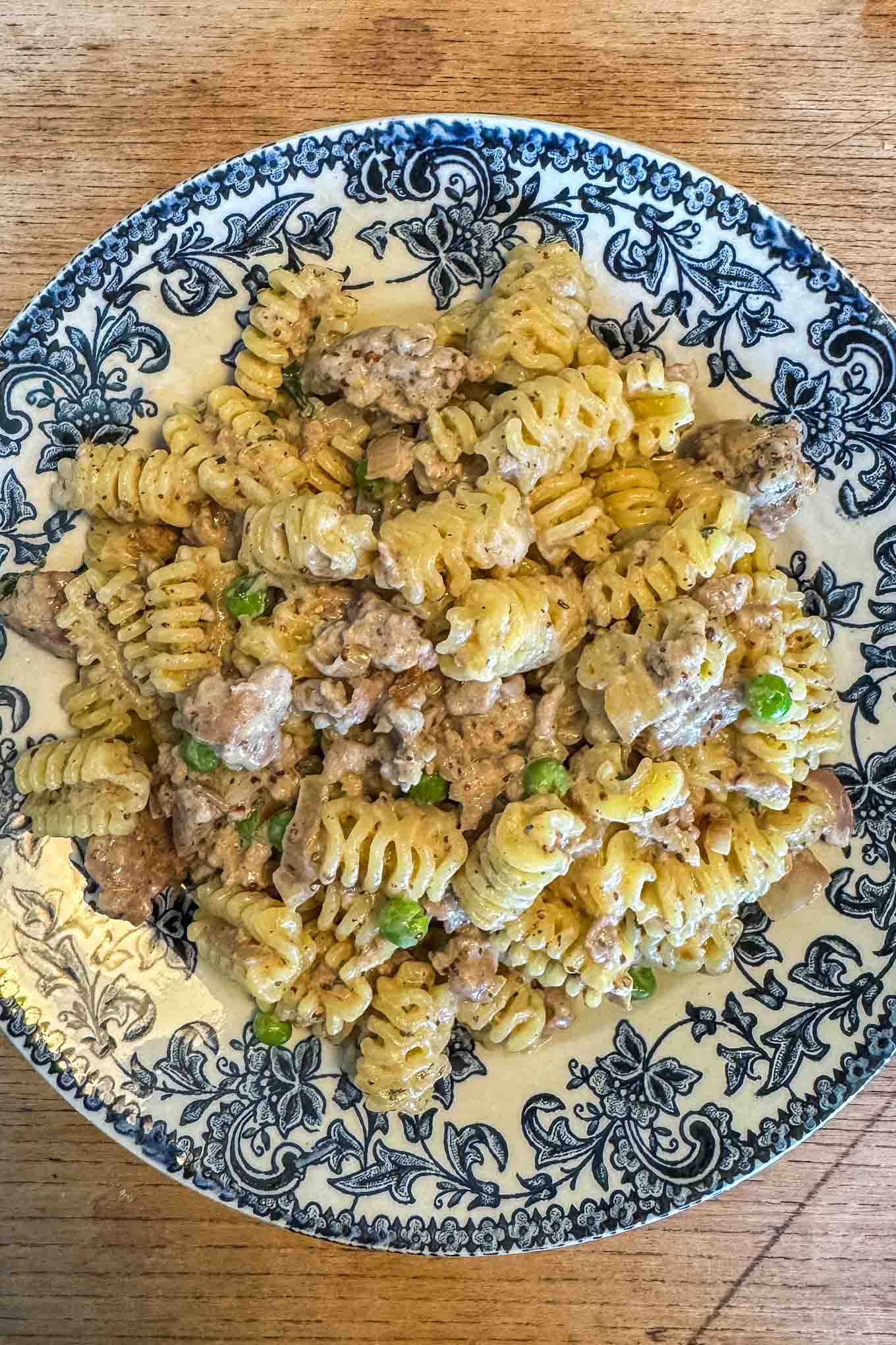 Plate of sausage mustard pasta with radiatori pasta, peas, and a creamy mustard sauce on a blue and white patterned dish.