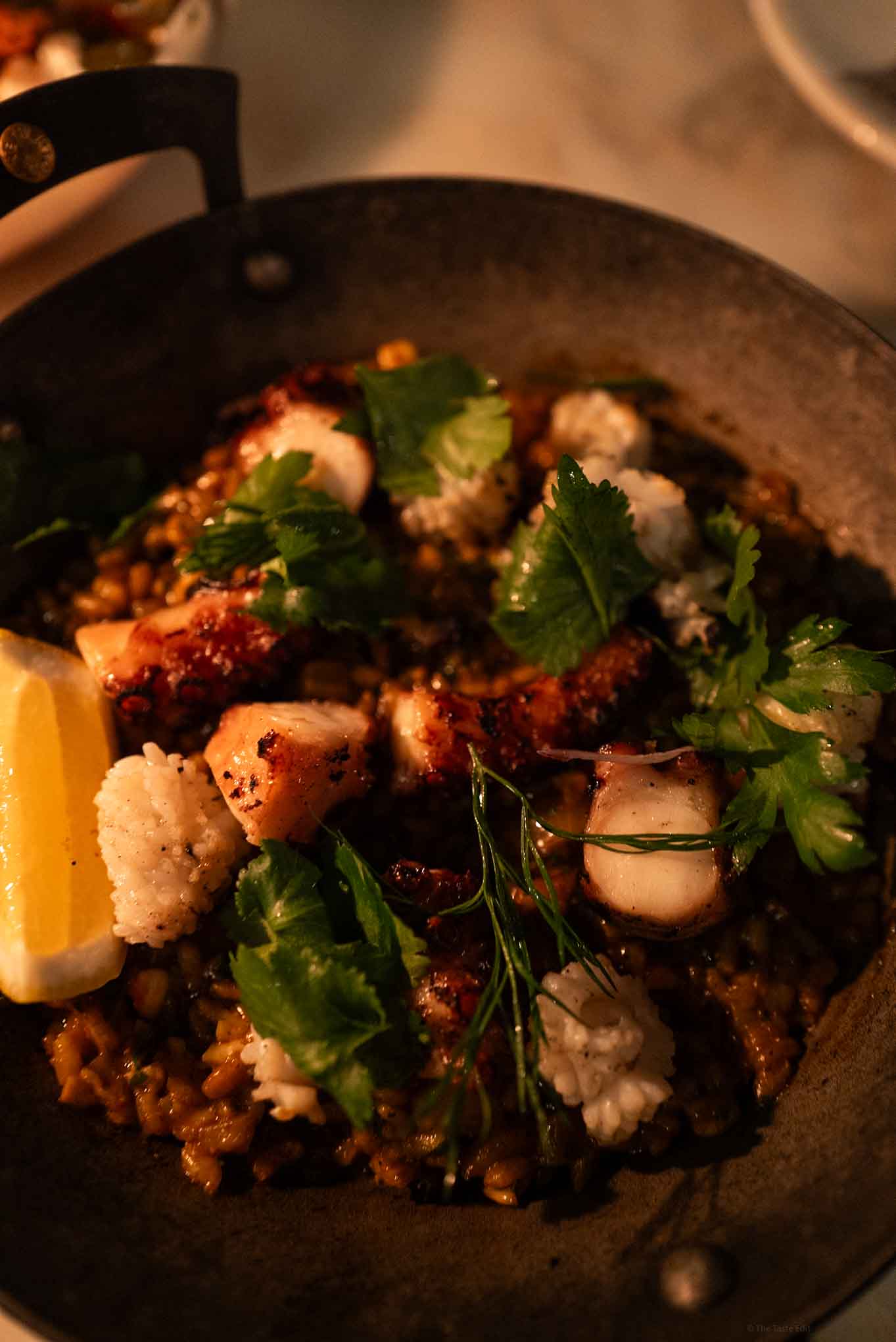 Octopus dish with herbs, lemon, and vegetables in a skillet.