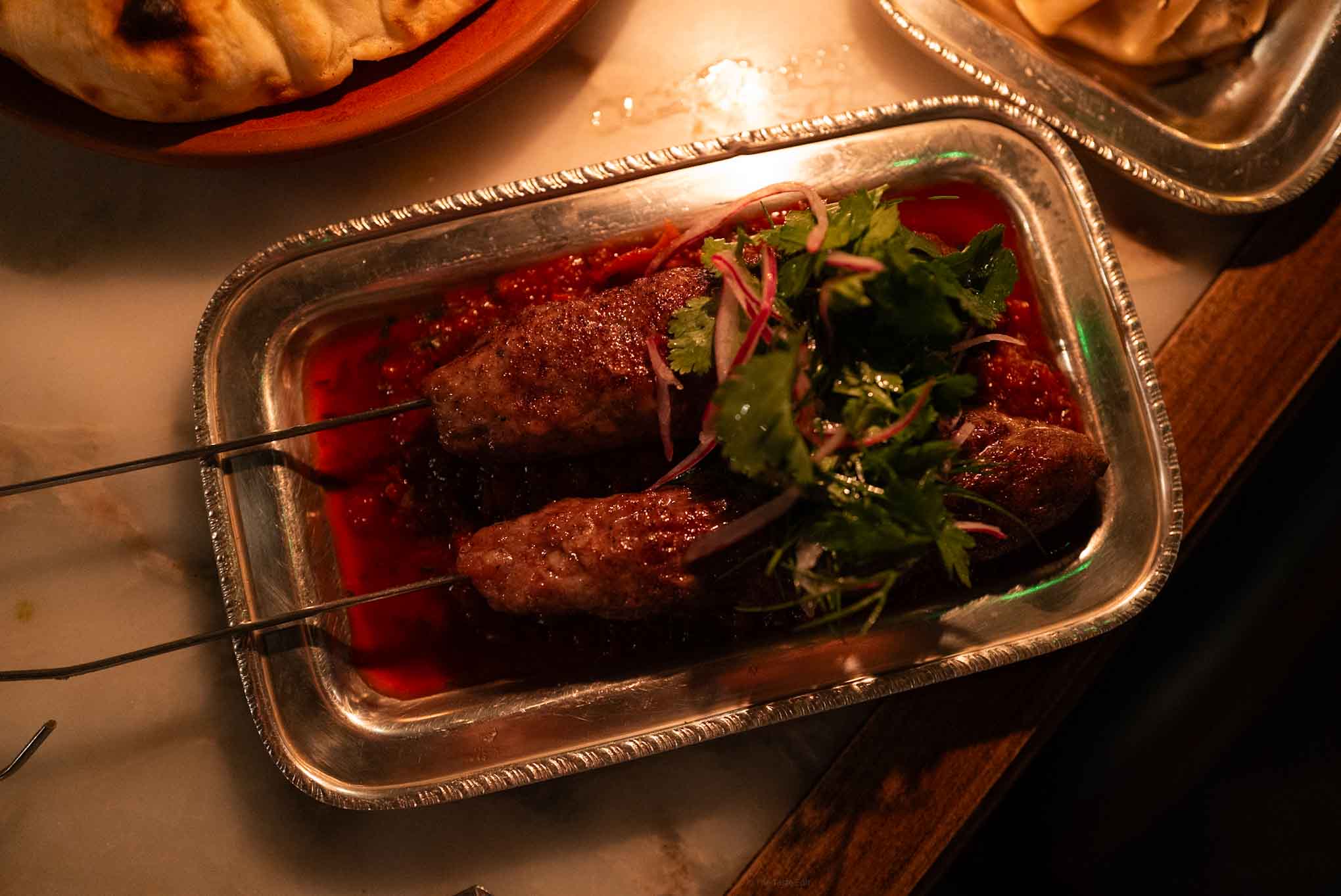 Delicious grilled meat skewers garnished with fresh herbs in a metal tray. Perfect for flavorful at Daka Daka in London a Georgian restaurant 