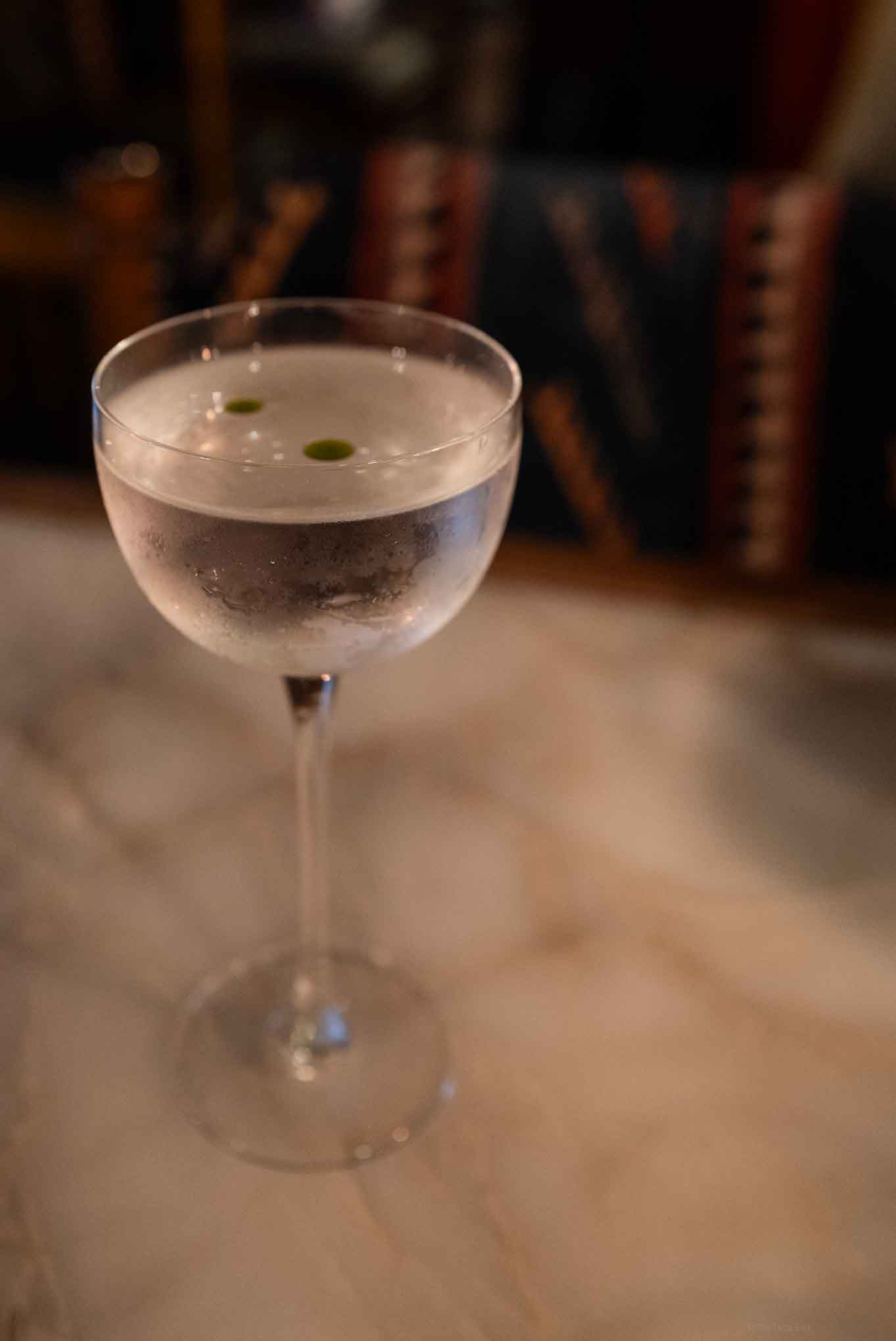 Elegant vesper martini cocktail with green garnish in a coupe glass on marble table.