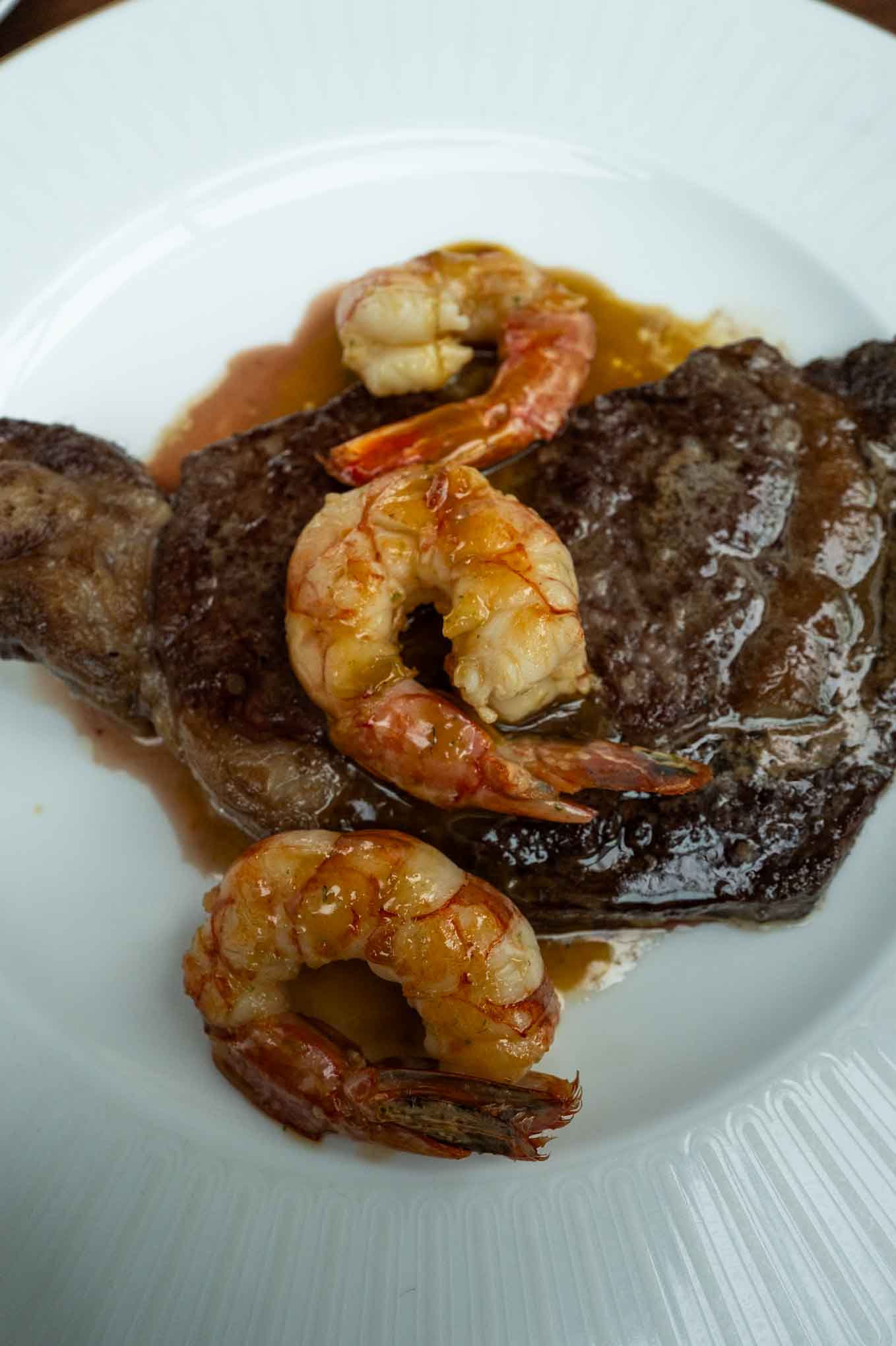 Delicious steak topped with shrimp, served with savory sauce on a white plate. Perfect for seafood a.