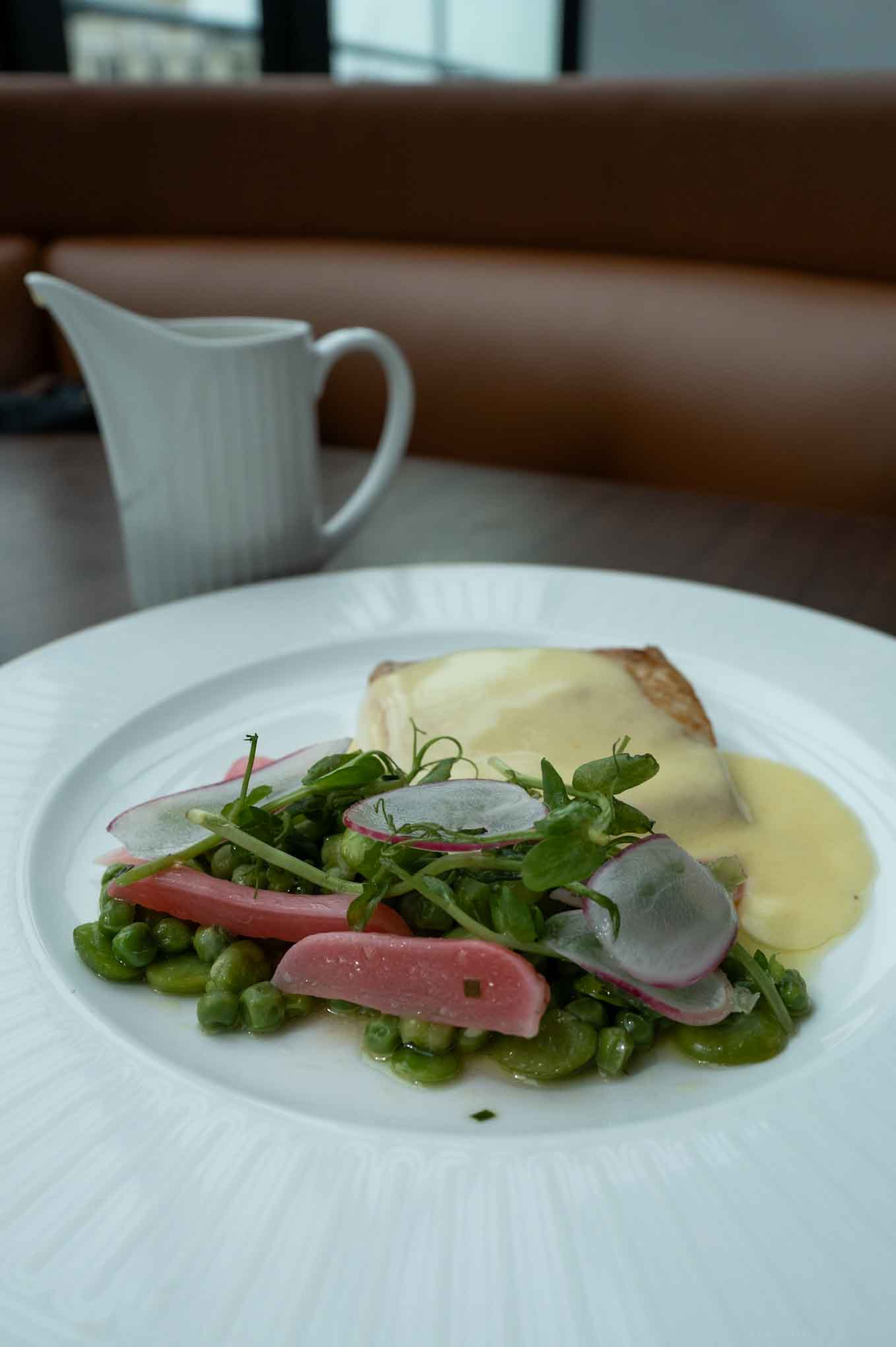 Fresh fish fillet with peas, radishes, and melted cheese on a white plate.