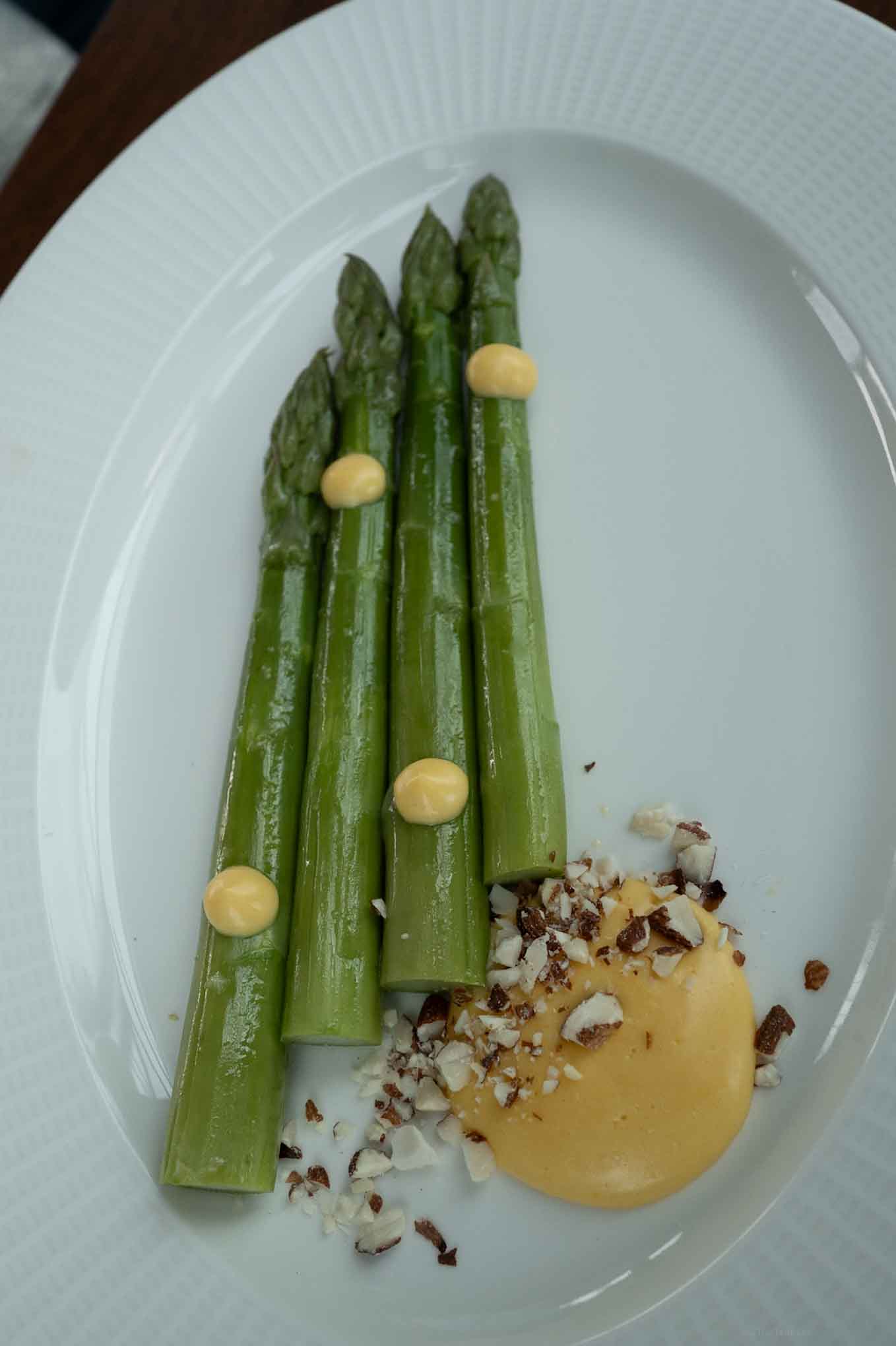 Fresh asparagus spears with lemon aioli drizzle and toasted nuts on a white plate.