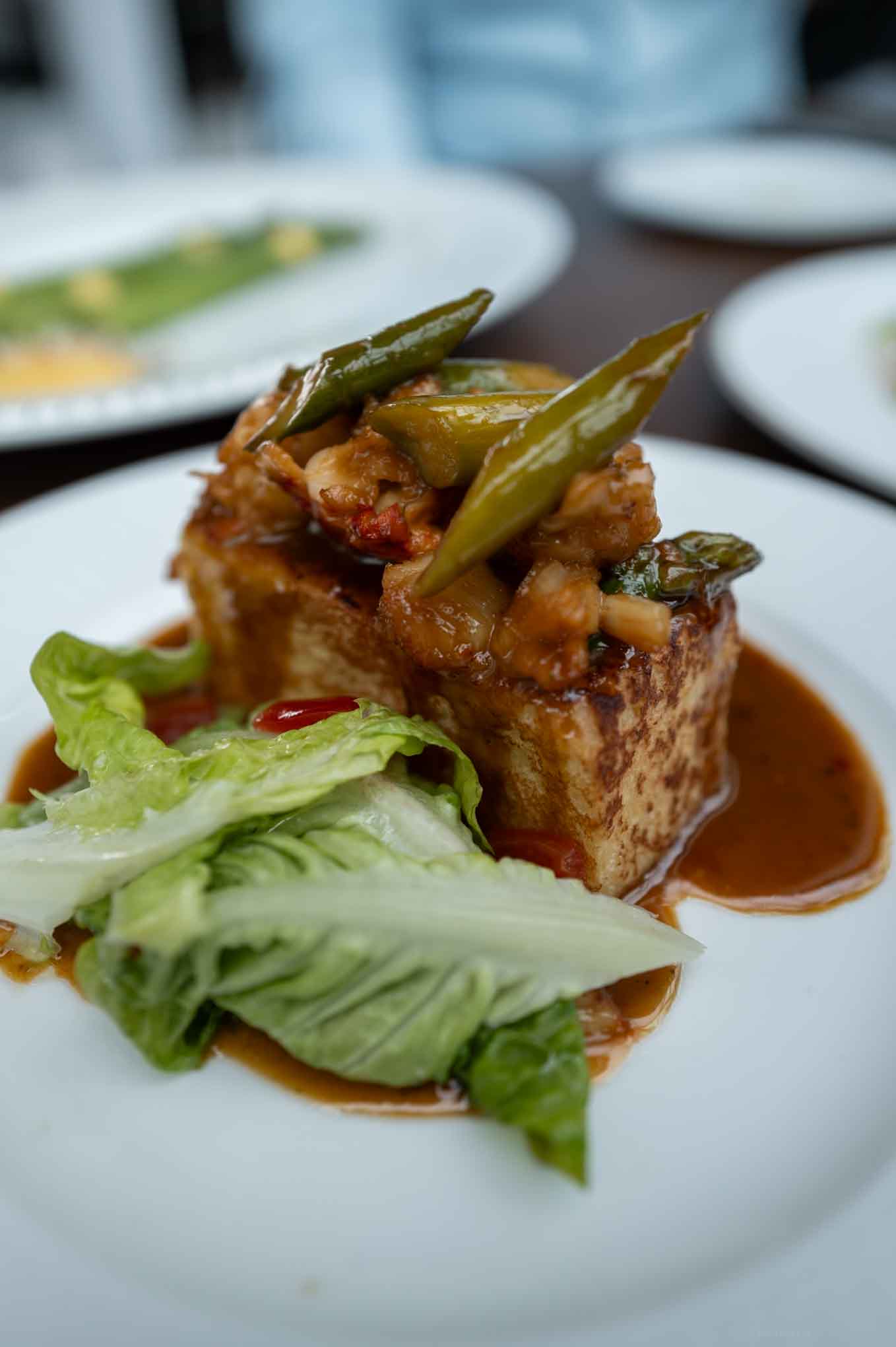 Delicious tofu dish topped with green beans and savory sauce, served with fresh lettuce on a white p.