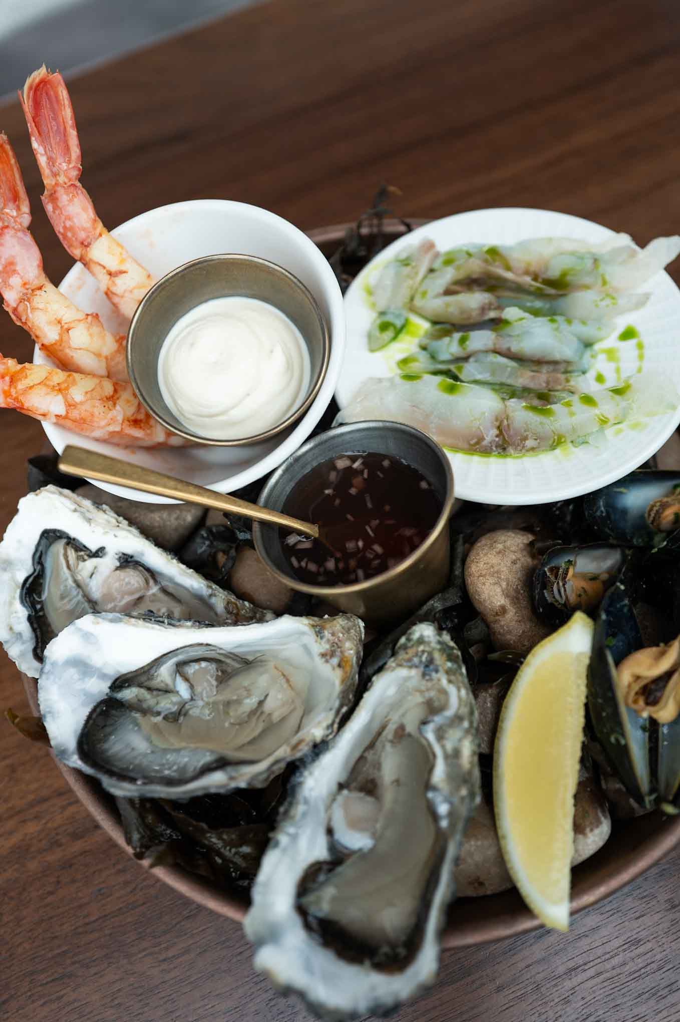 Seafood platter with oysters, shrimp, mussels, lemon, and dipping sauces for a seafood feast.