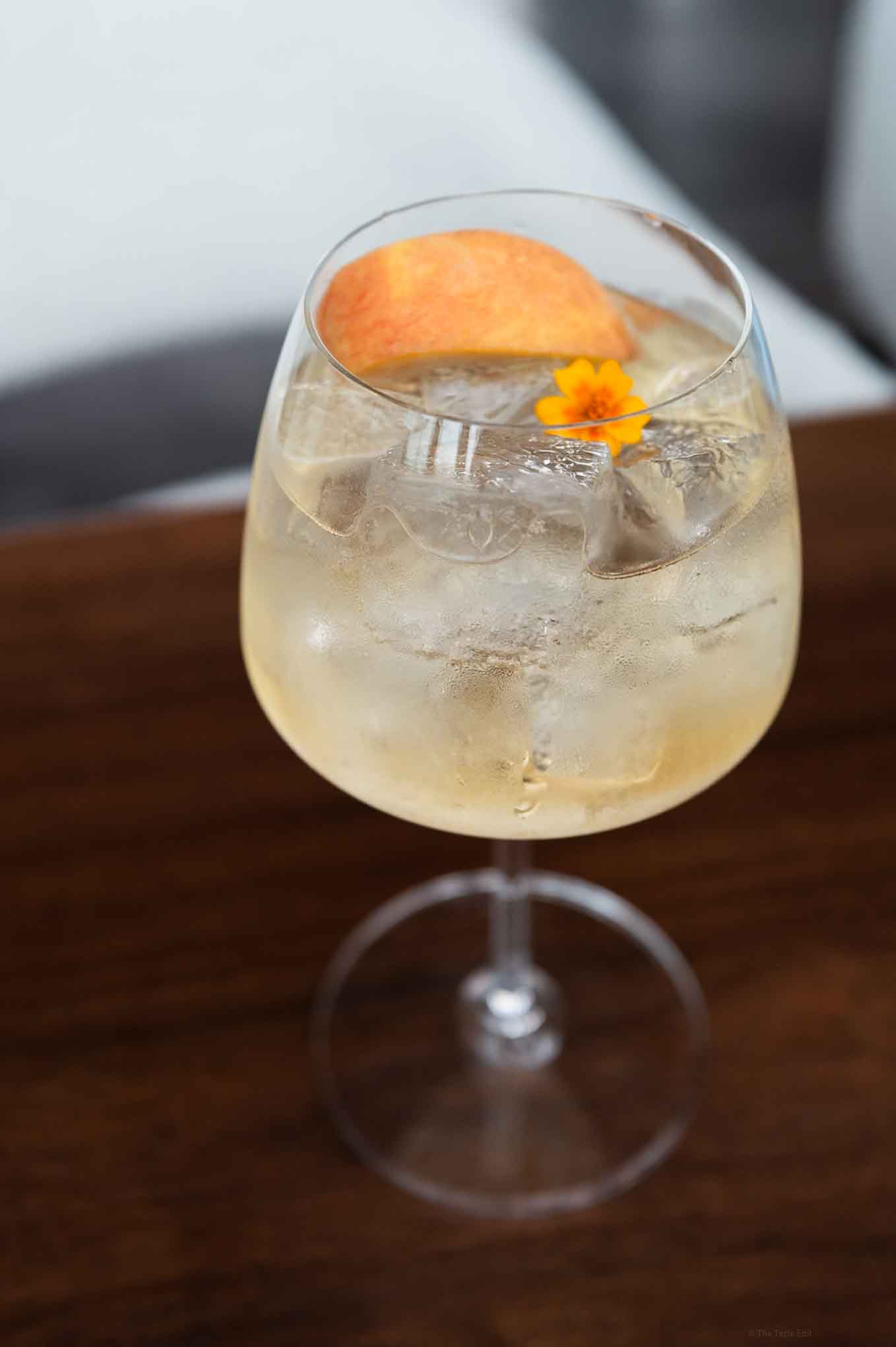 Refreshing citrus cocktail with orange slice and edible flower garnish.