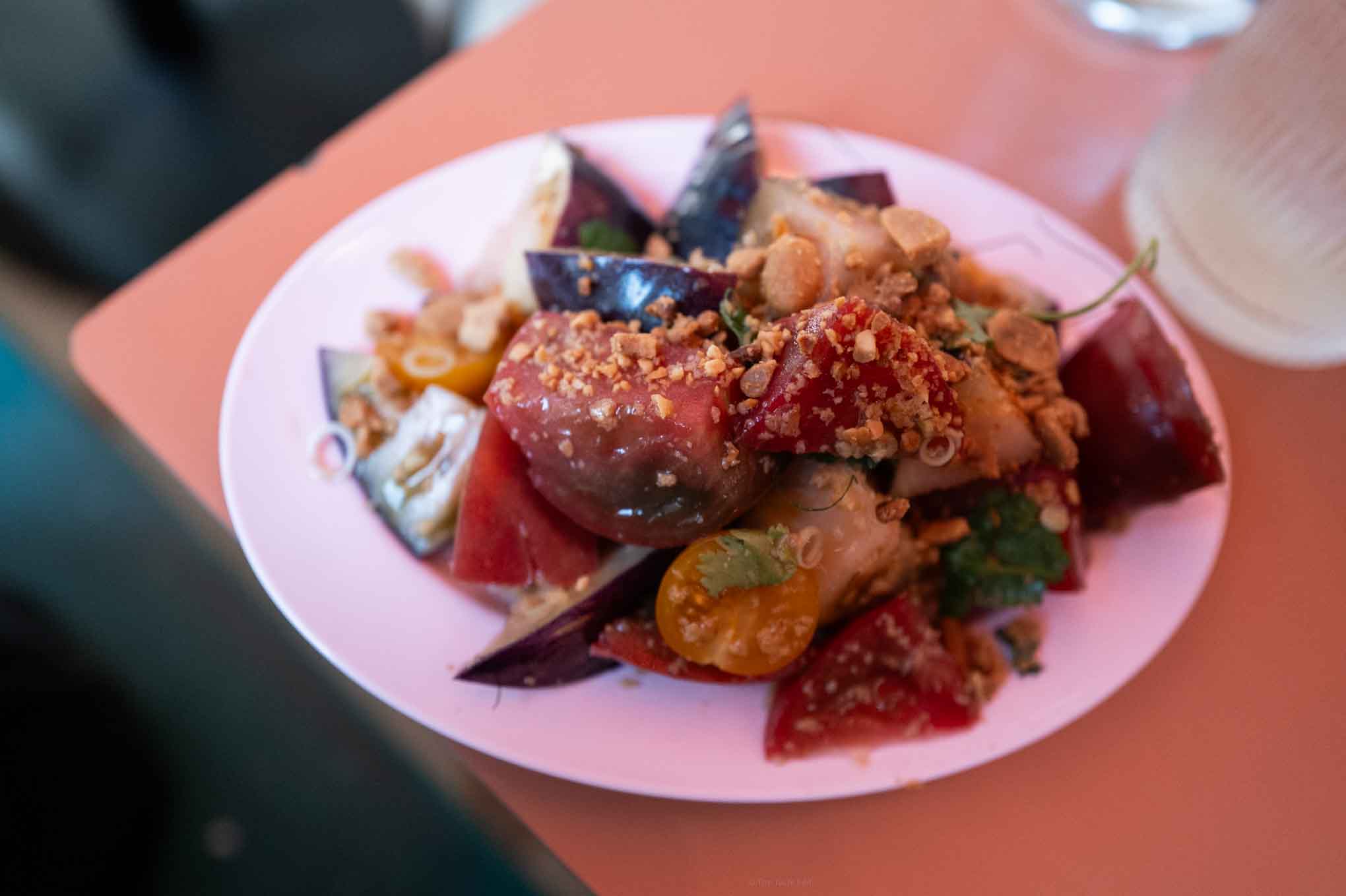 Thai tomato salad with vegetables, herbs, and crunchy toppings on a white plate.