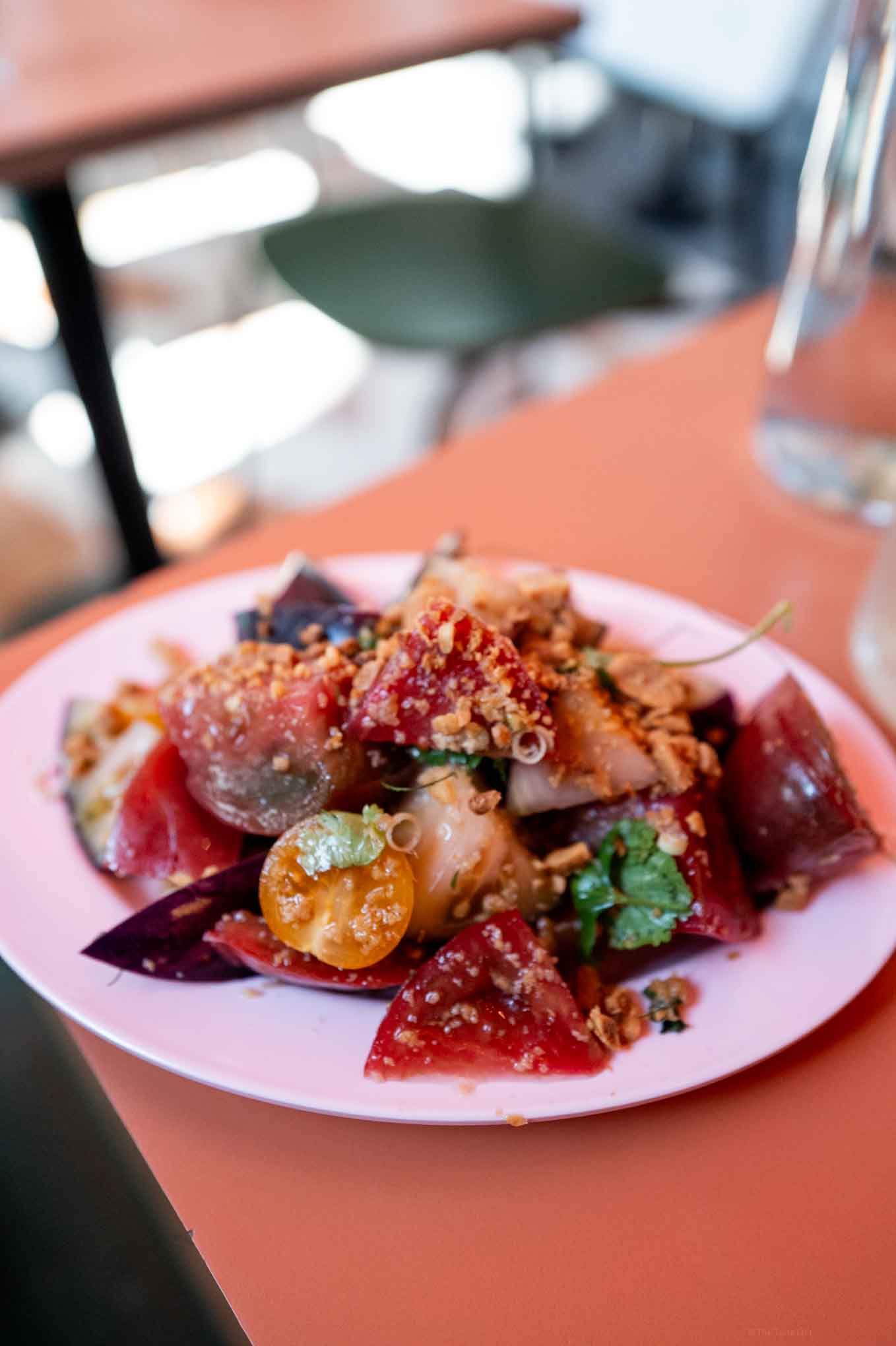 Fresh Thai tomato salad with greens, crunchy toppings, and vibrant colors on a pink plate.