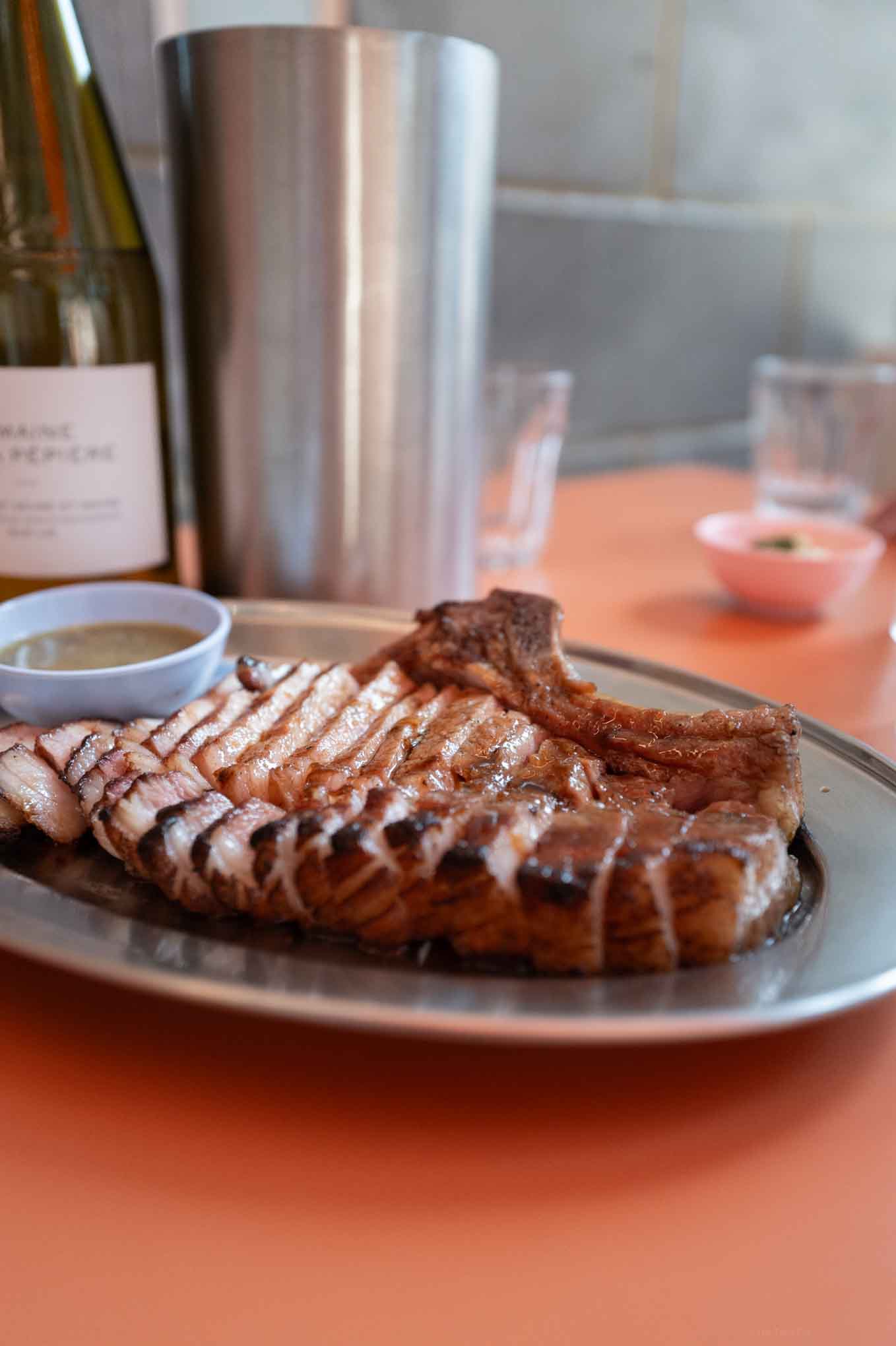 Juicy grilled pork chop served with dipping sauces on a restaurant plate.