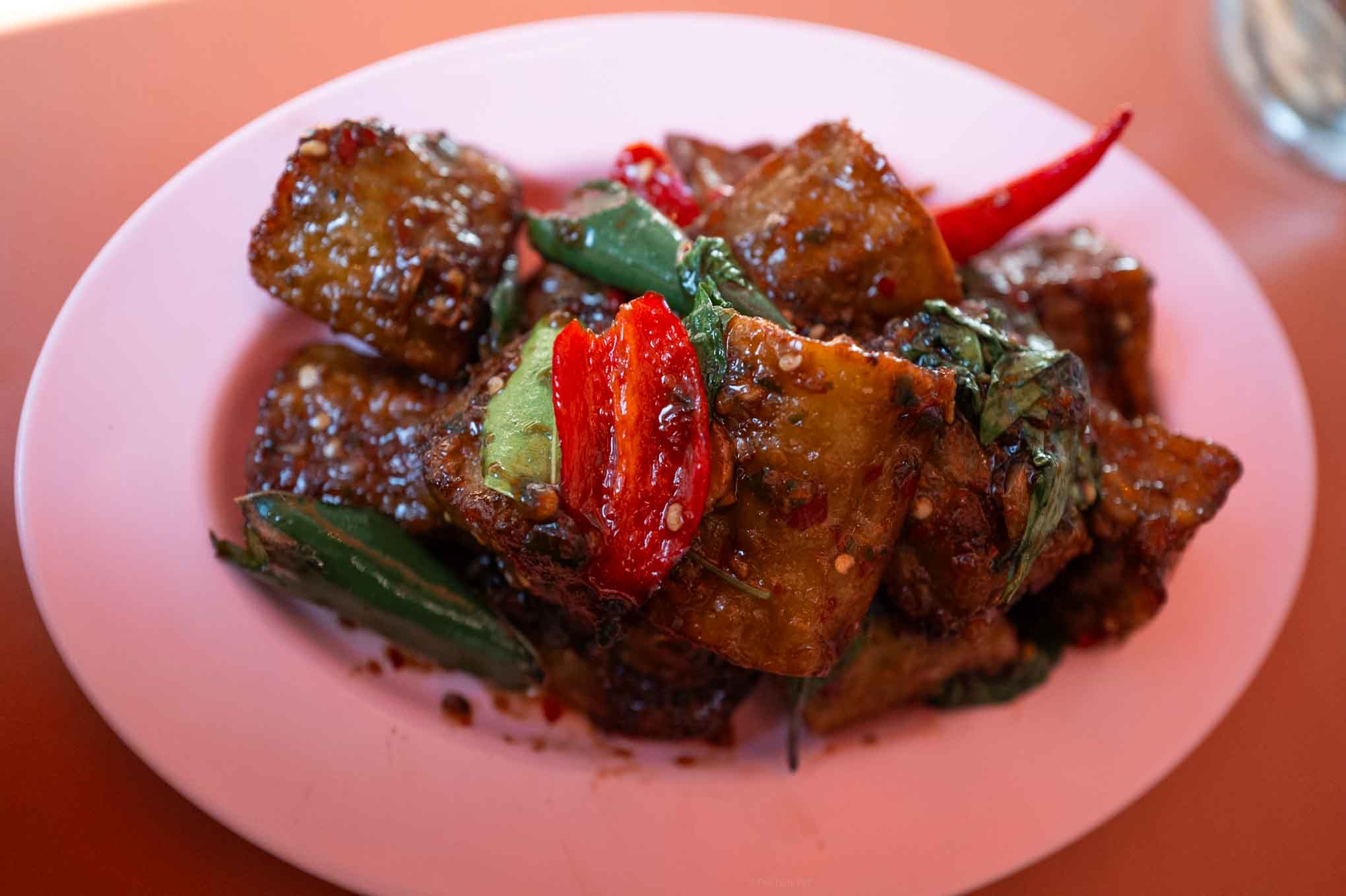 Spicy eggplant with colorful peppers and greens on a pink plate. Perfect for healthy, flavorful.