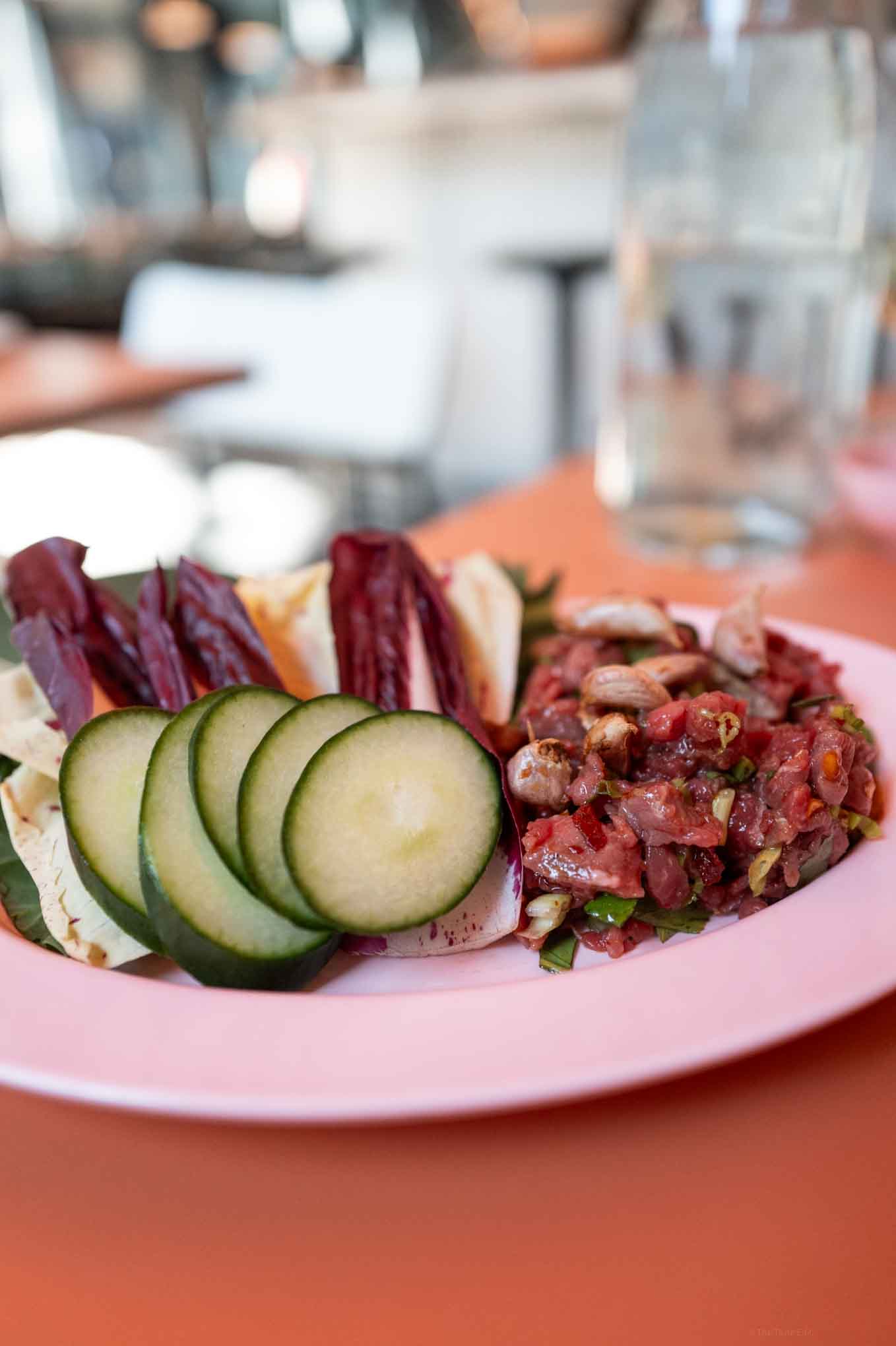 Raw Thai beef platter with cucumbers, radicchio, and tomato salad on a pink plate. Perfect for hea.