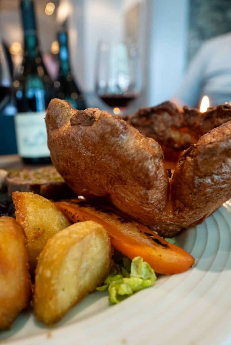 Didn’t Yorkshire puddings with juicy roast beef served with roasted potatoes, carrots, and fresh greens on a dinner plate.