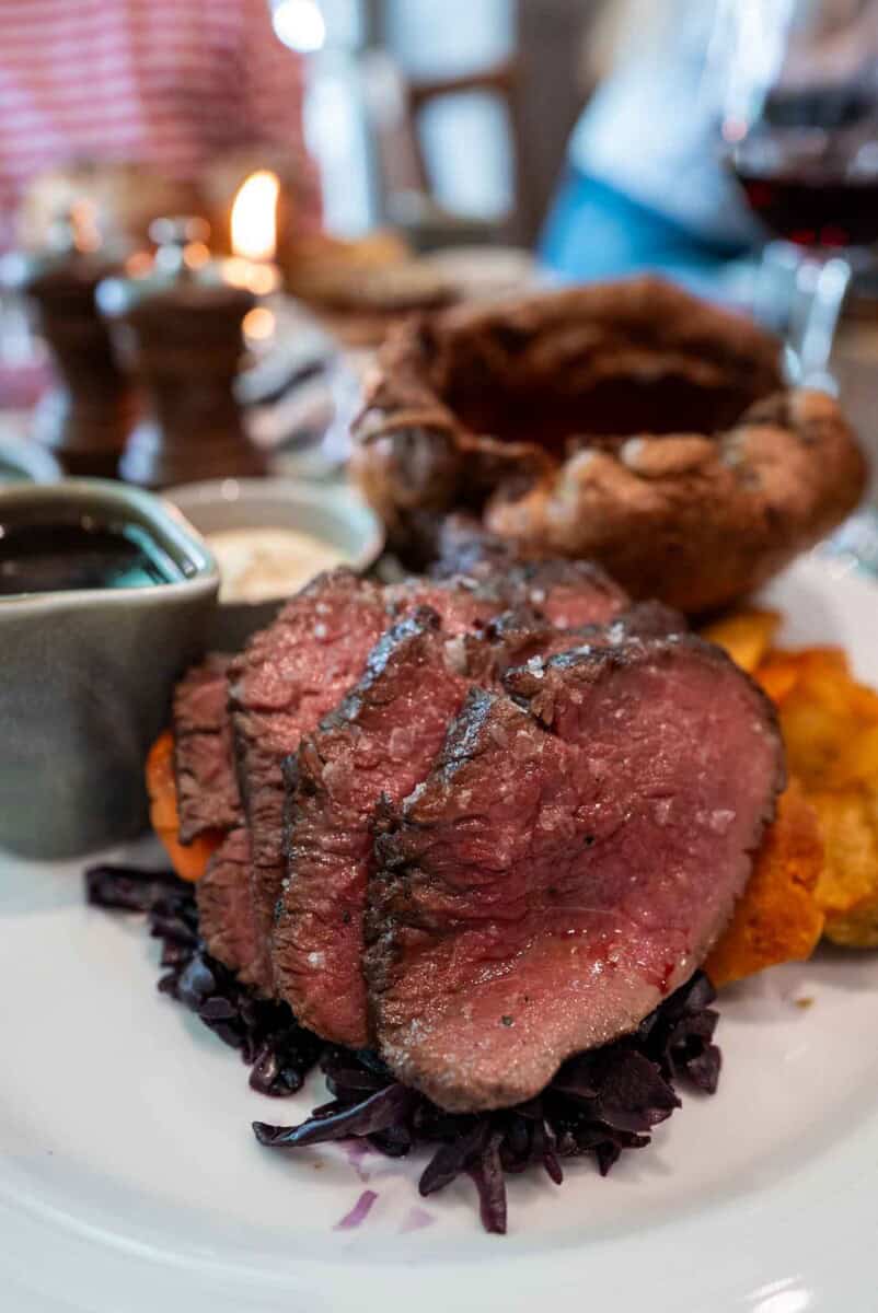 Juicy grilled steak served with roasted sweet potatoes and cabbage on a white plate and giant yorkshire pudding for a Sunday roast in London at Brook and Badger Pub .