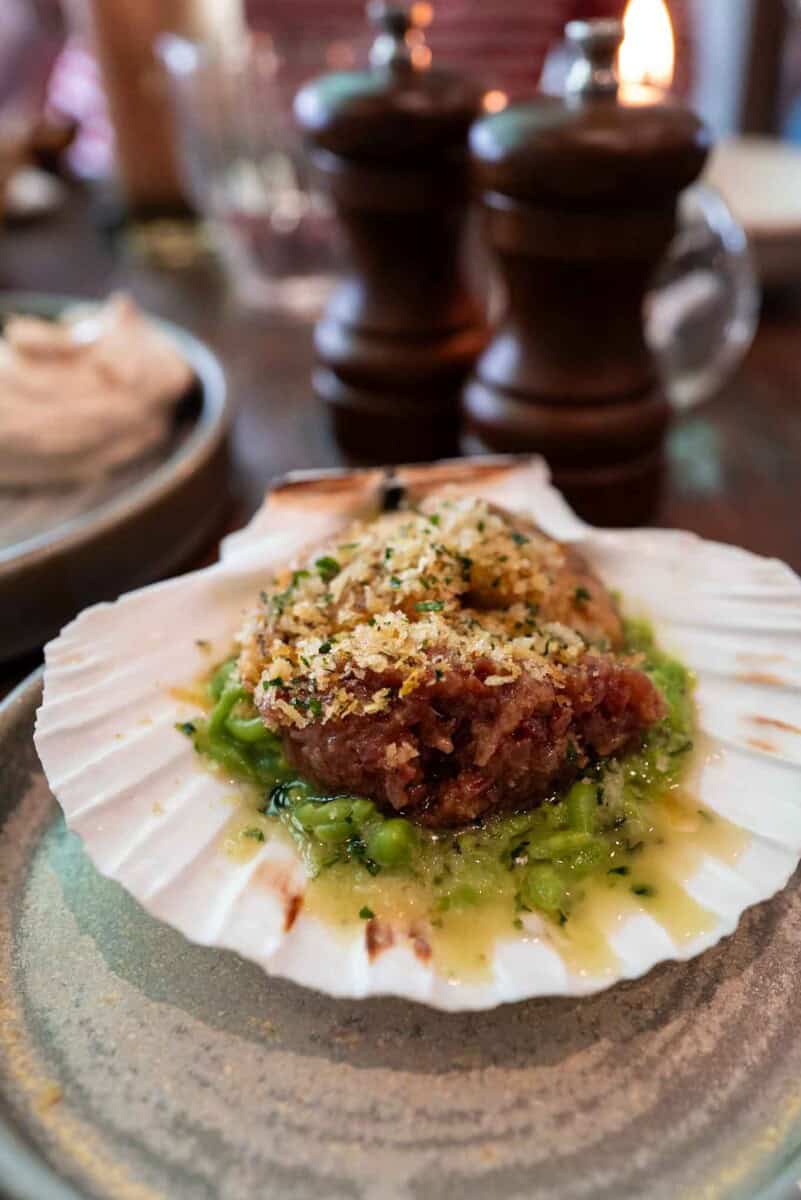 Delicious baked scallop served on a shell with breadcrumb crust and vibrant green sauce made of mushy peas, served at brook and badger
