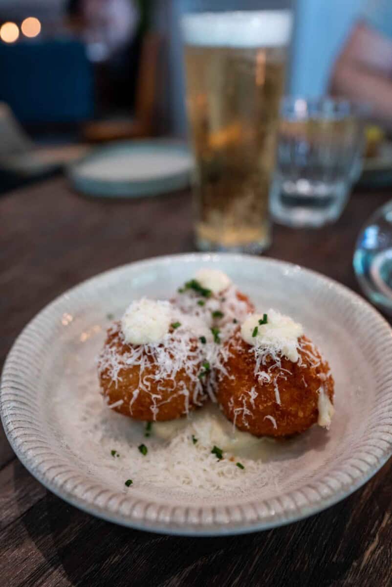 Crispy fried croquettes with ham - cheese balls garnished with Parmesan cheese and herbs on a white plate.