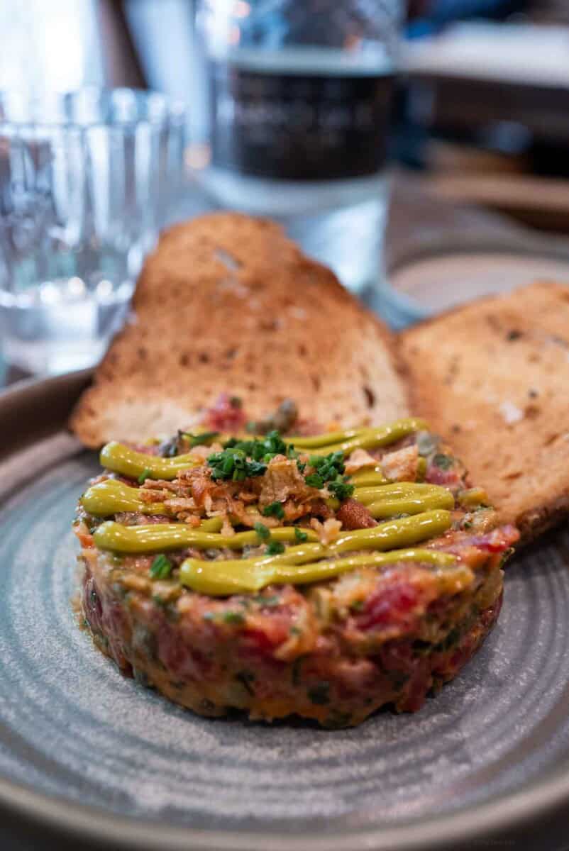 Steak tartare topped with green beans, served with toasted bread slices on a stylish plate at a brook and badger pub in London.