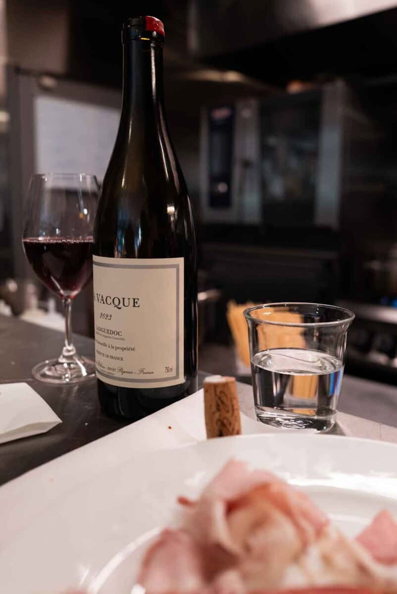 Elegant red wine bottle with glass of red wine and water glass on kitchen counter.