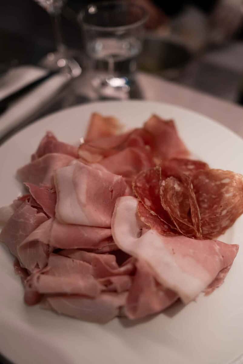 Cured meats including prosciutto, salami, and ham on a white plate. Perfect for charcuterie boards a.