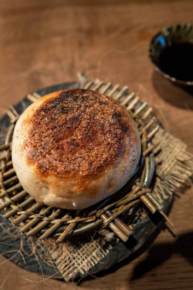 Steamed Chinese bun with crispy, caramelized top and soft interior, served on a woven bamboo tray.