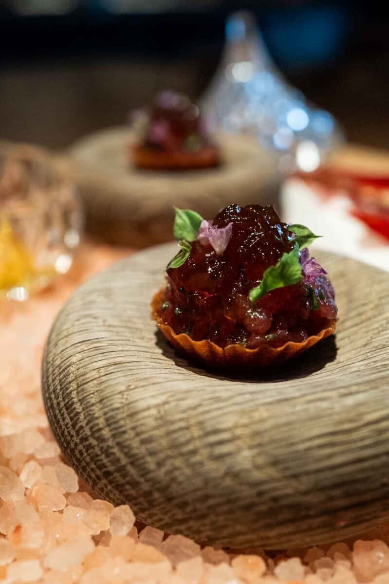 Mini fruit tart with berry jam and fresh mint on a textured stone surface.