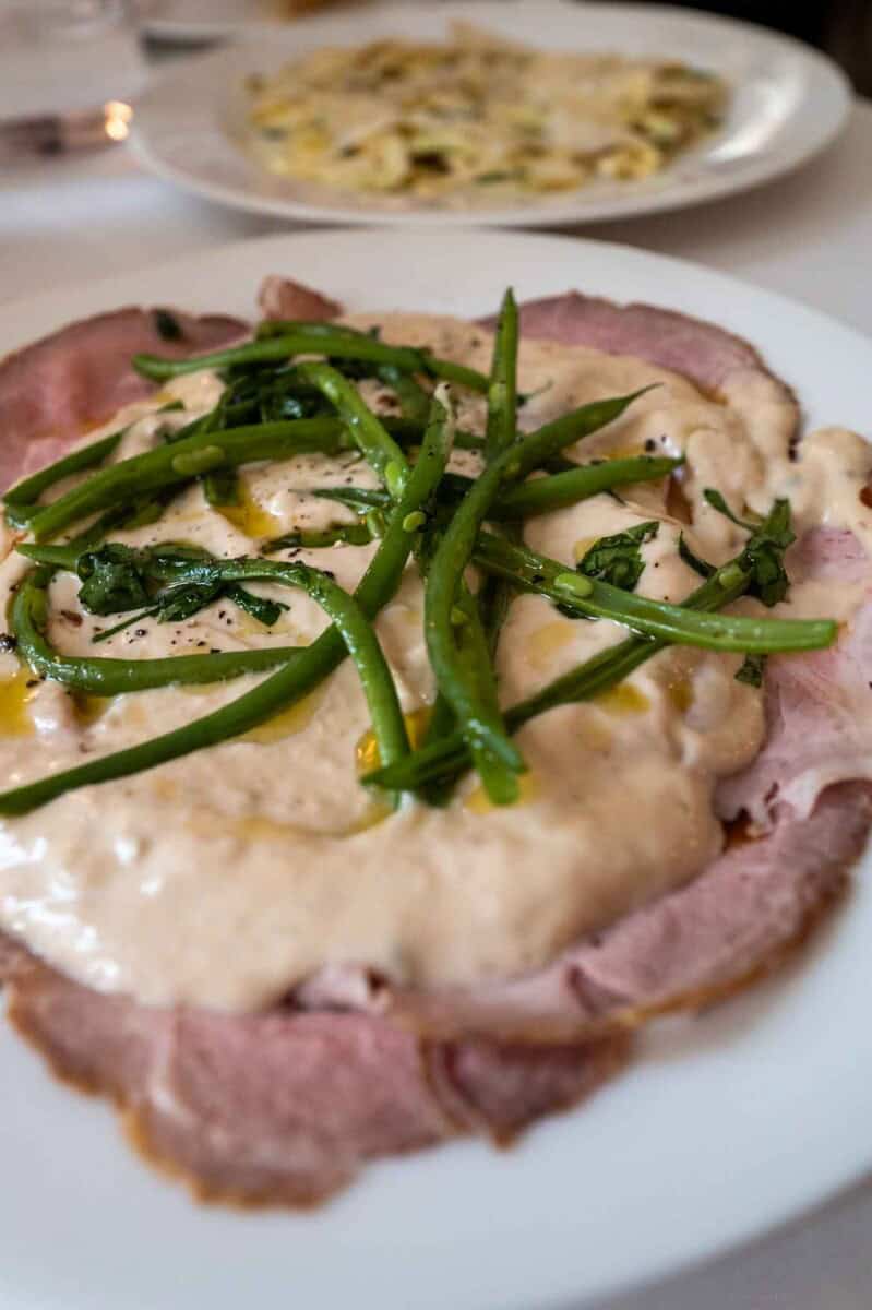 Green bean and ham casserole with creamy sauce on a white plate.