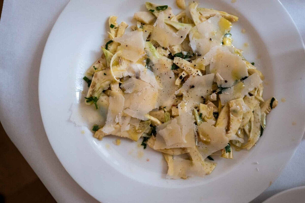 Shaved raw artichoke and Parmesan cheese salad on a white plate.