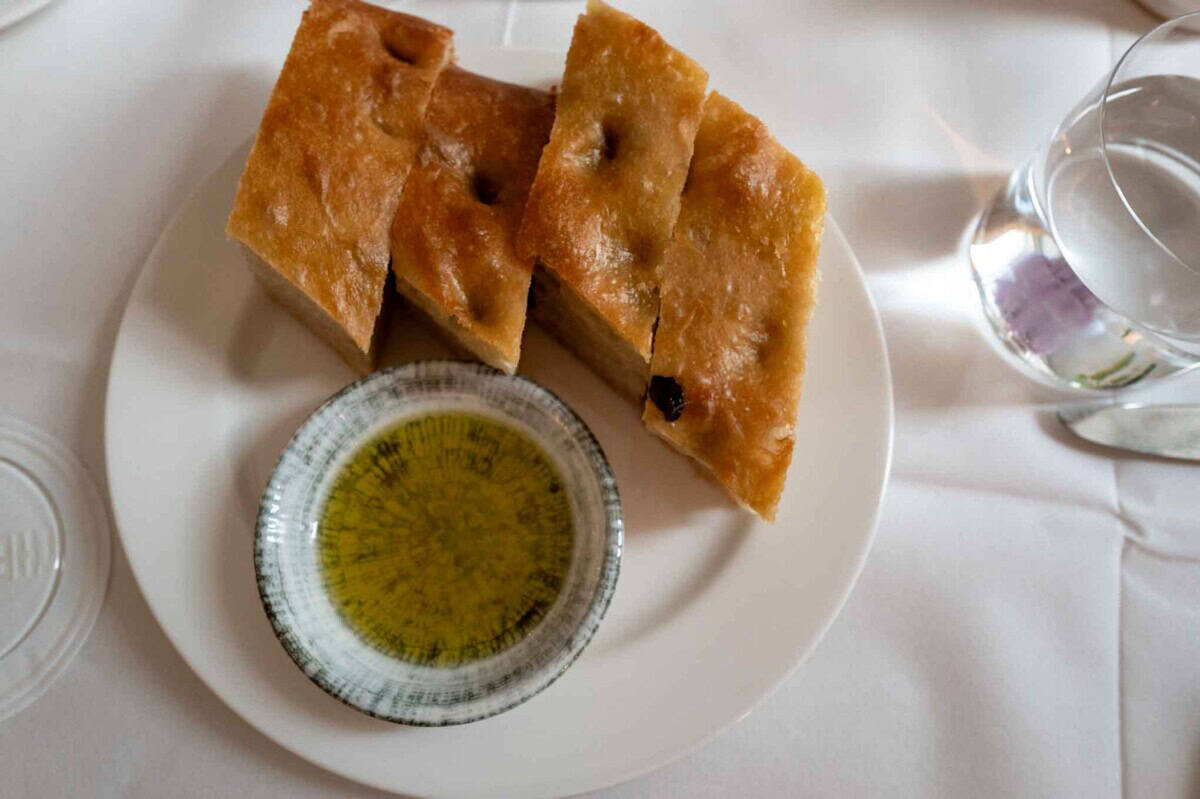 Fresh focaccia bread with olive oil dipping sauce on a white plate.