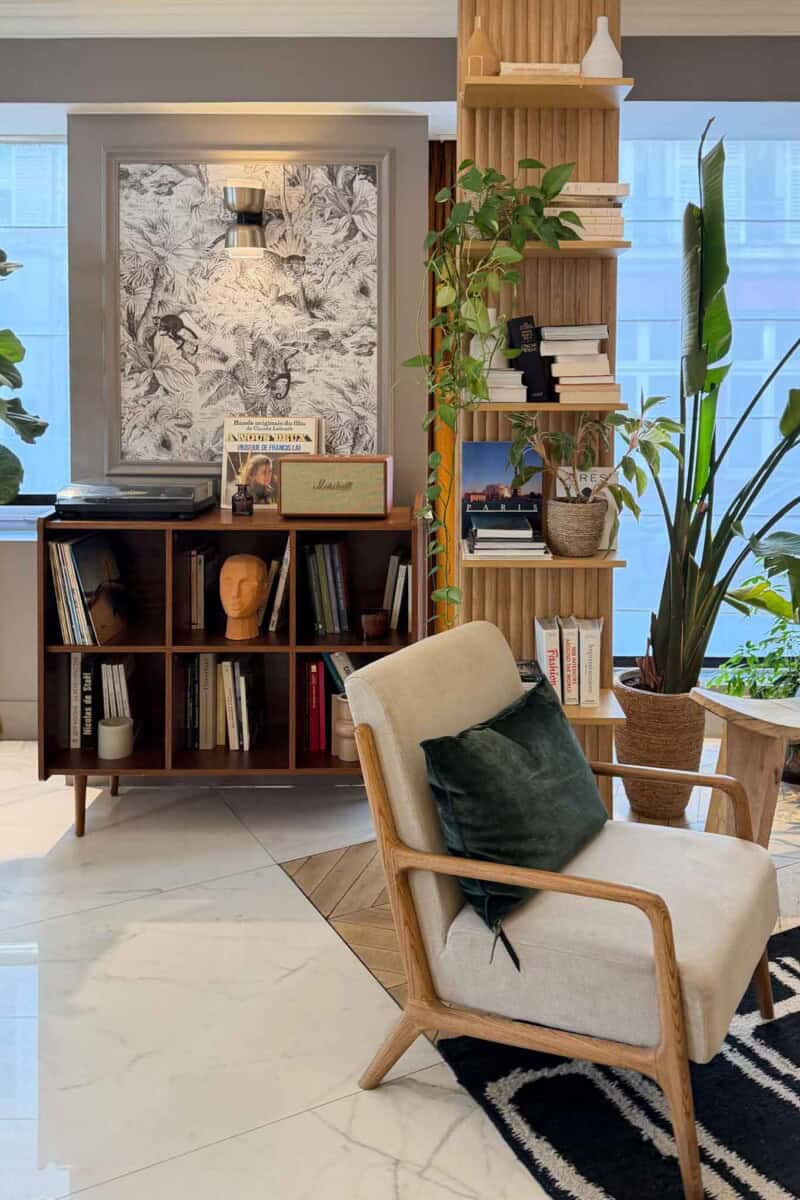 Stylish living room corner with bookshelf, armchair, and lush greenery.