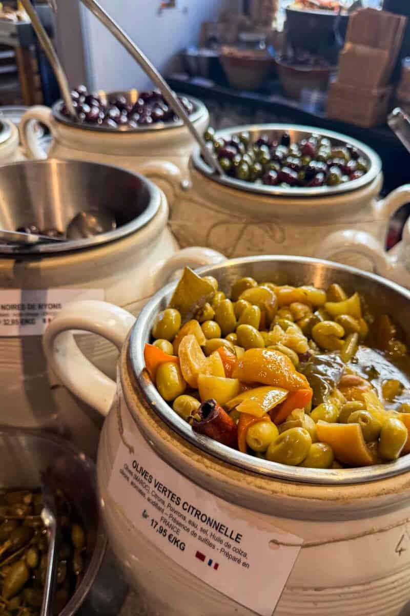 Vibrant green and black olives with grapes served in rustic ceramic bowls at a market.