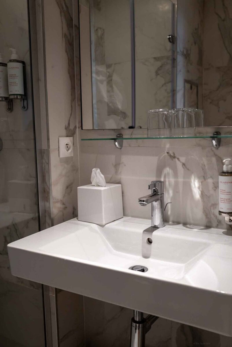 Modern bathroom sink with mirror, tissue box, and toiletries in a stylish marble setting.