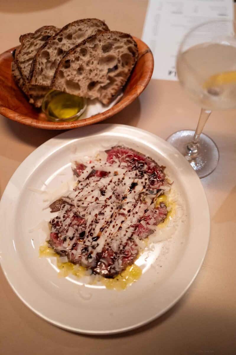 Beef carpaccio drizzled with olive oil, herbs, and balsamic glaze, served with toasted bread and a l.
