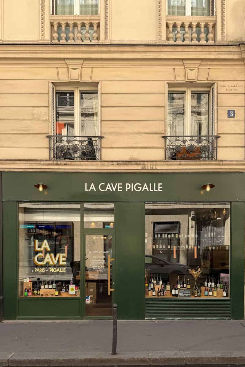 Exterior view of La Cave Pigalle, a cozy Paris wine shop with elegant green facade and display windo.