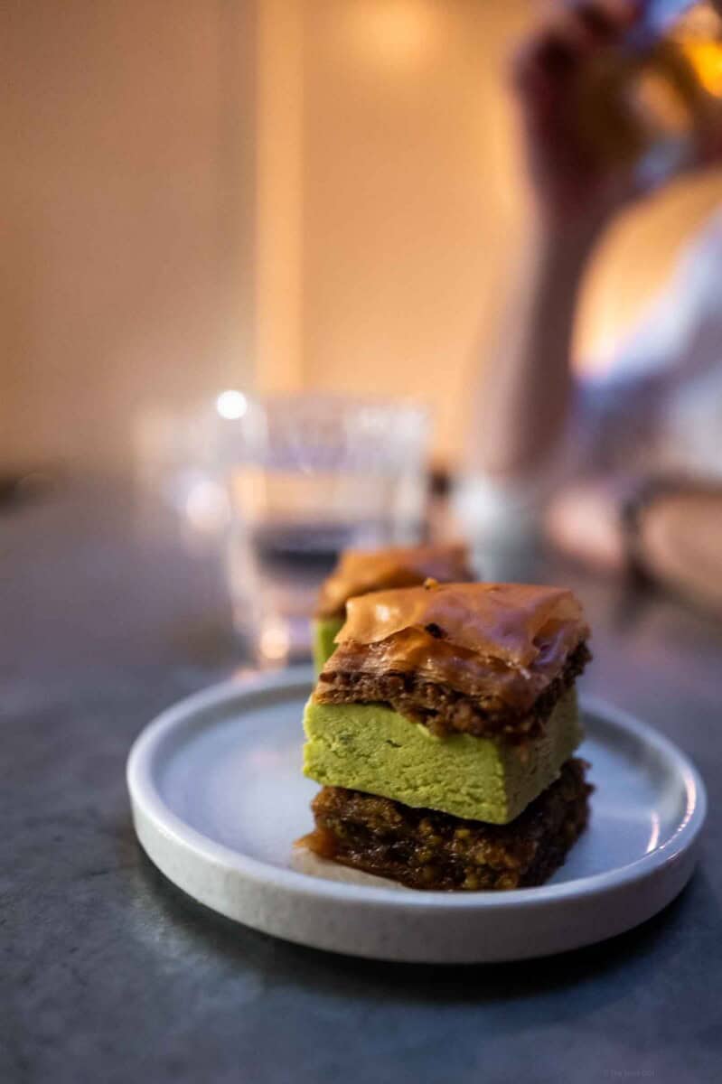 Close-up of a layered matcha green tea dessert with caramel topping on a white plate.