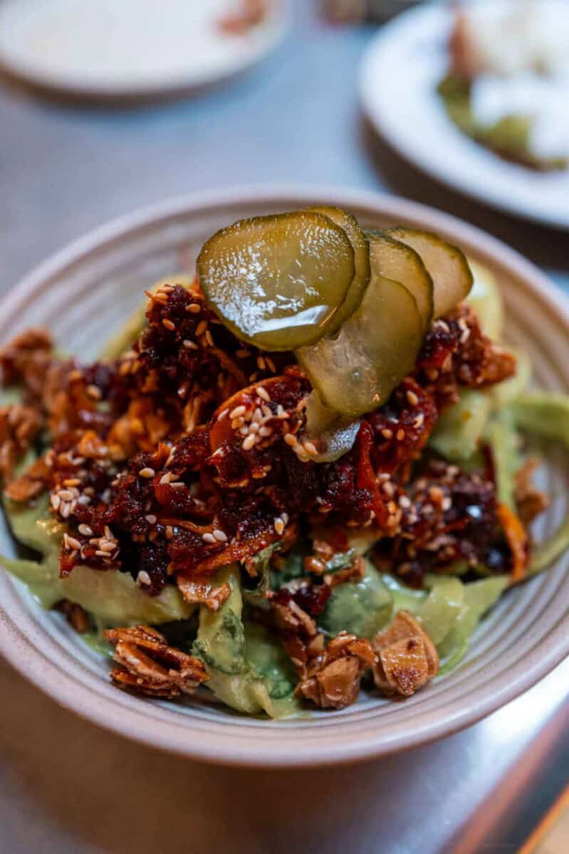 Delicious guacamole topped with pickles and crunchy garnishes in a rustic bowl.