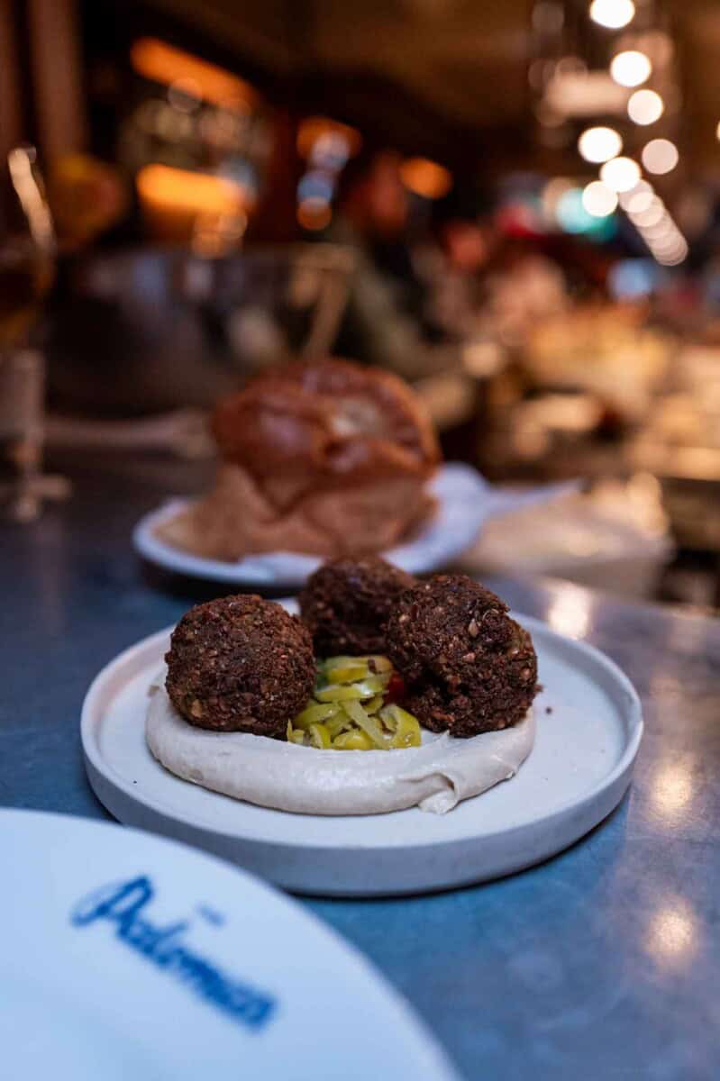 Gourmet meatballs served with pickles on a flatbread, in a lively restaurant setting.