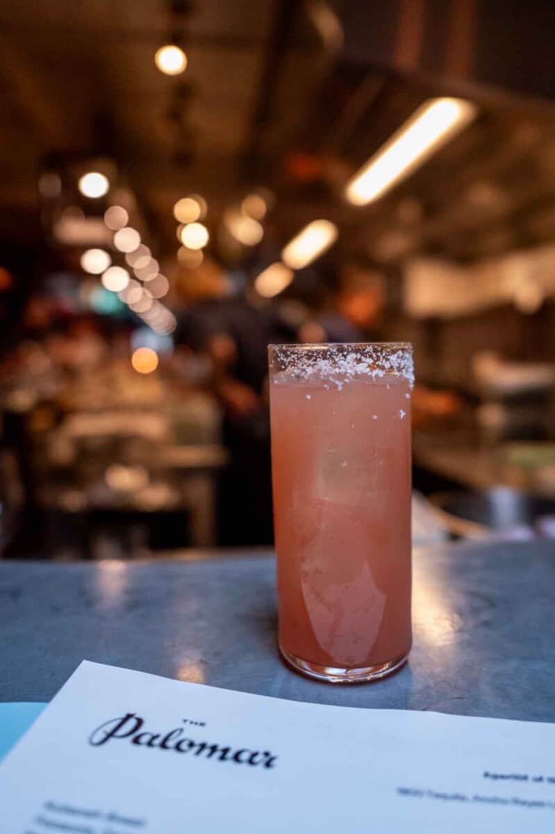 Elegant pink cocktail in a tall glass with salted rim at a trendy bar setting.