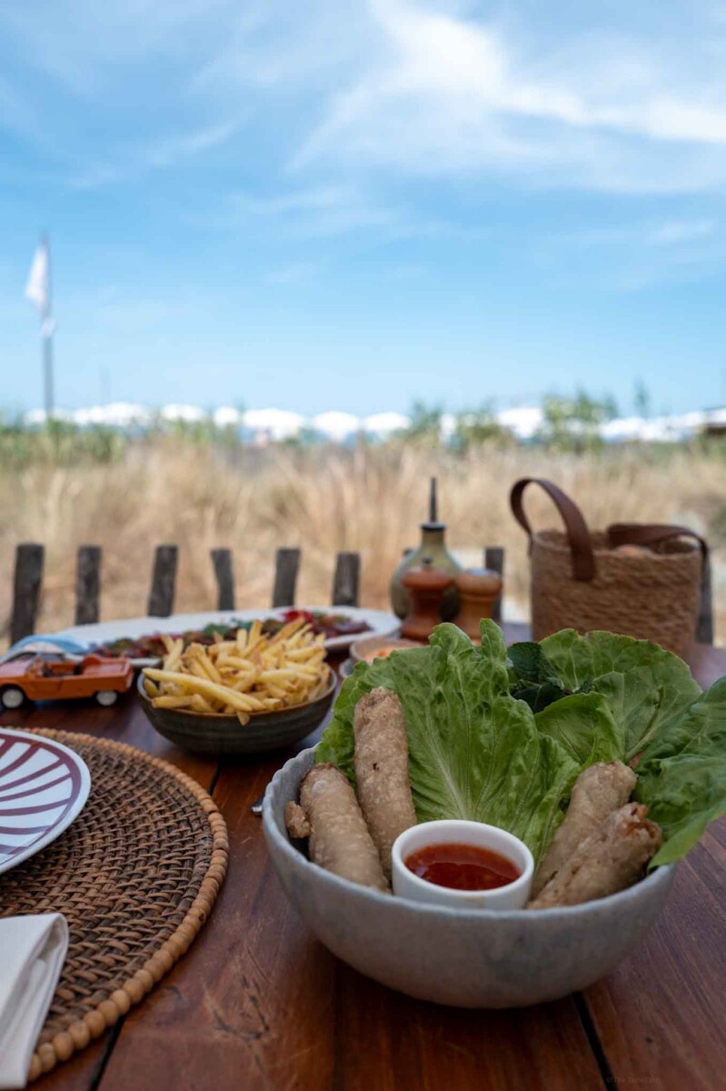 Fresh spring rolls with lettuce and dipping sauce on a beachside table.