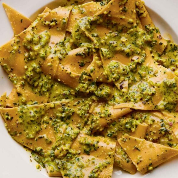 Homemade pasta with vibrant green pesto sauce on a white plate.